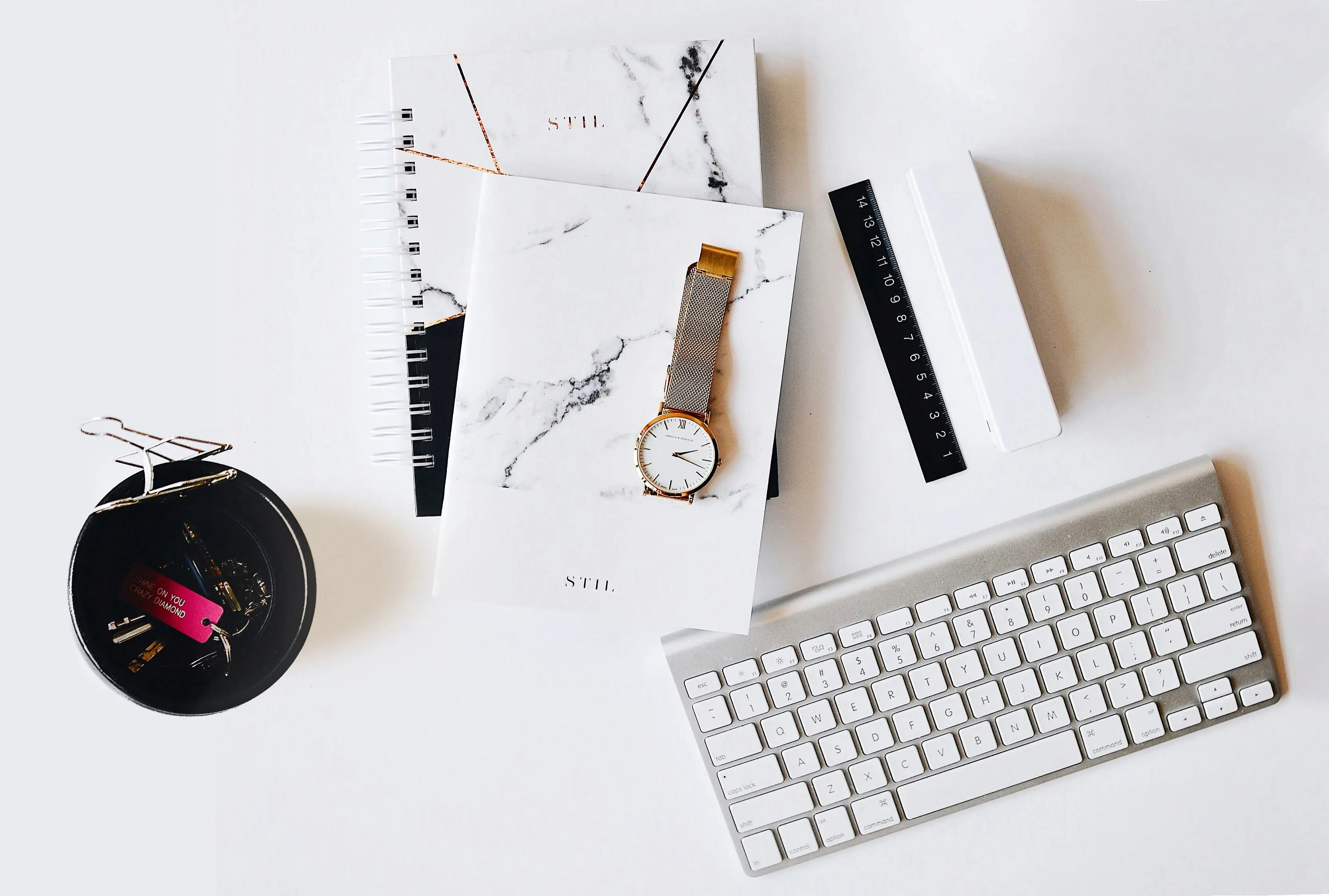 Presentation image with two notebooks, hand watch, ruler and Apple keyboard placed on a white surface.