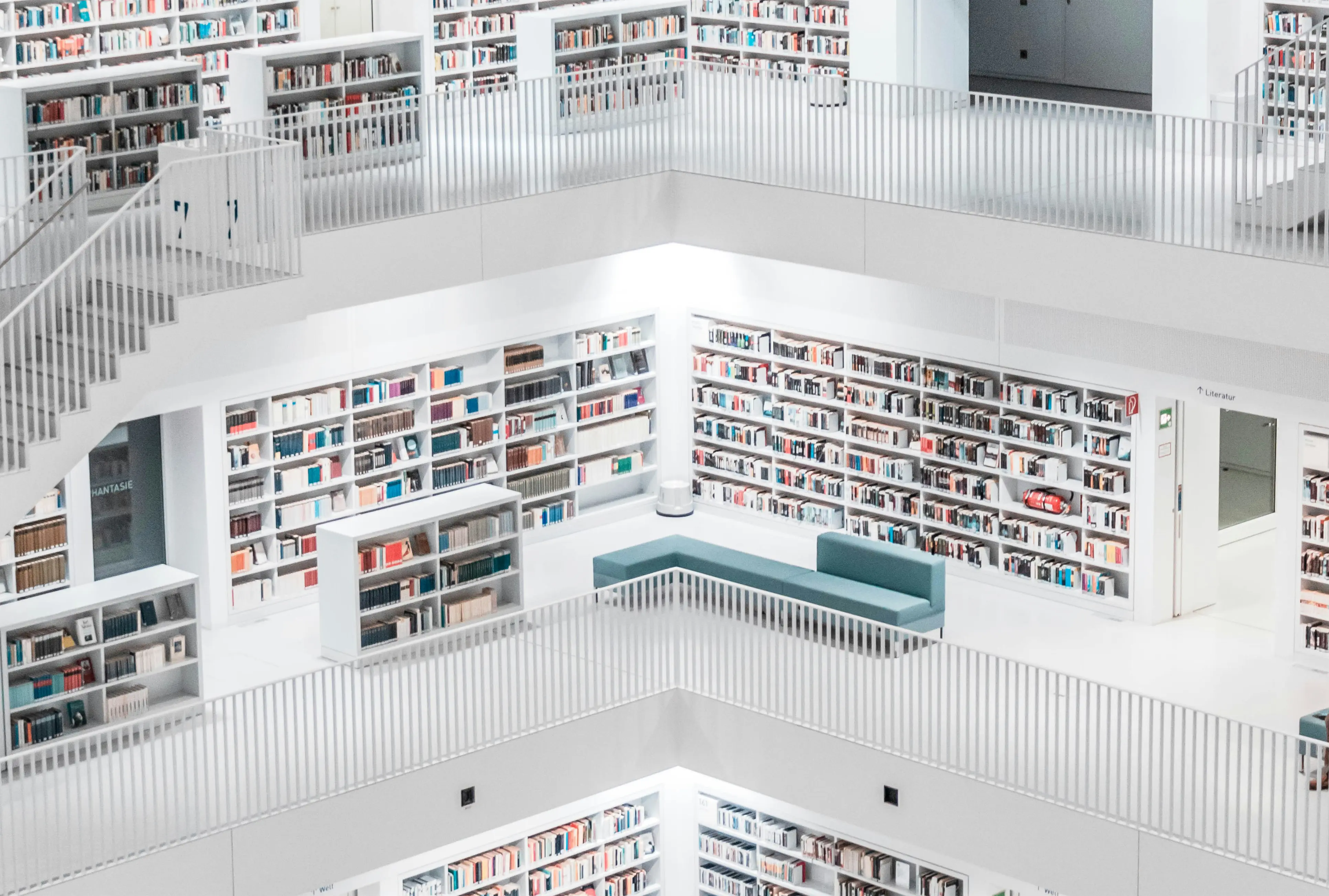 Presentation image of a multiple-story white-themed library, with floor-to-ceiling shelves of colorful books and a green L-shaped sofa.